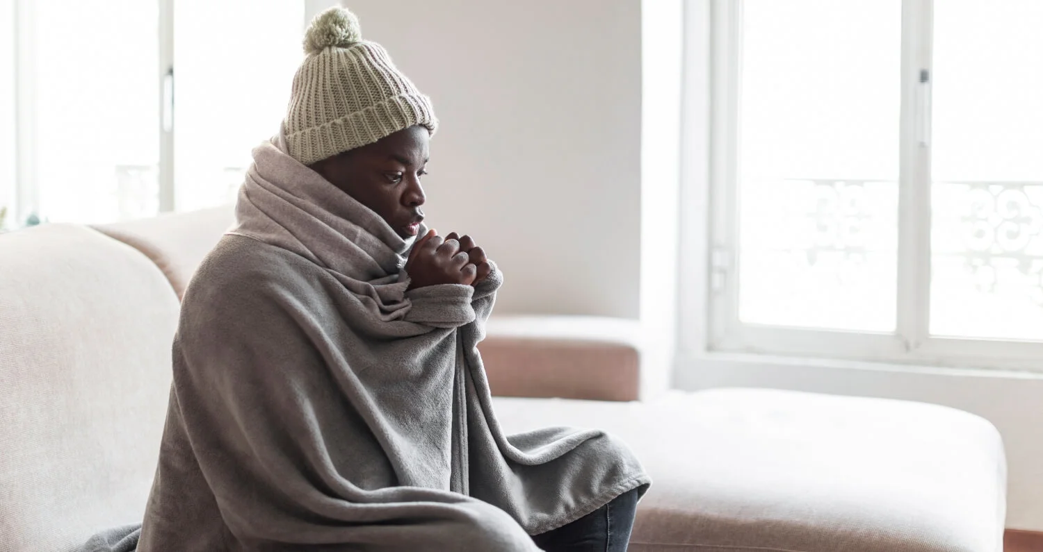 Young African American male sitting on a couch with a beanie and blanket