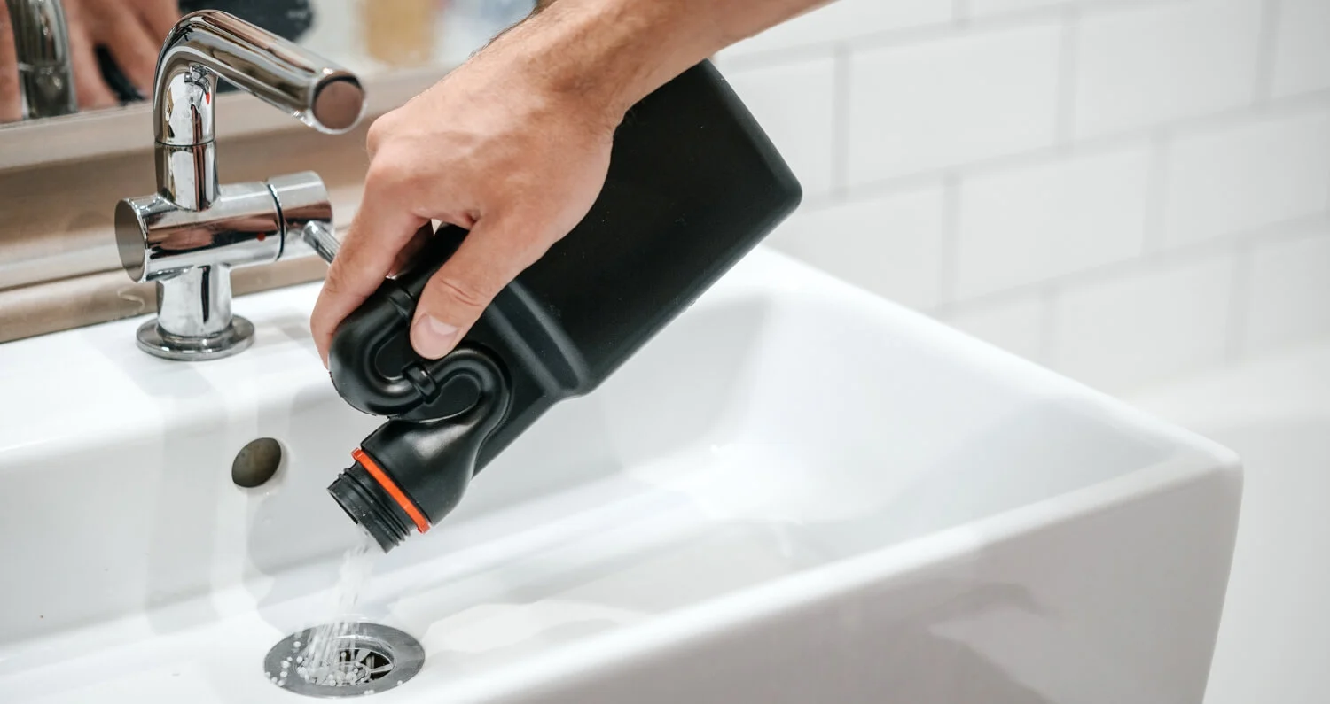 A man pours drain cleaner down the drain of a bathroom sink.