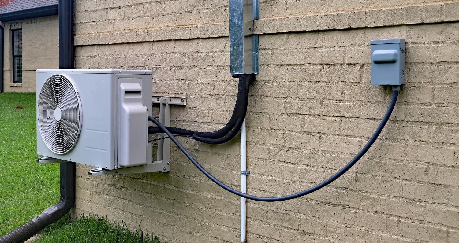 A ductless electric heat pump mounted on a brick wall.